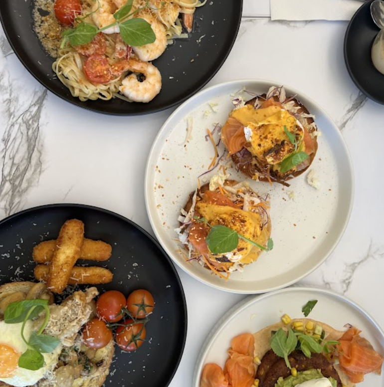 Brunch plates on marble: prawn pasta, salmon eggs benedict, breakfast plate