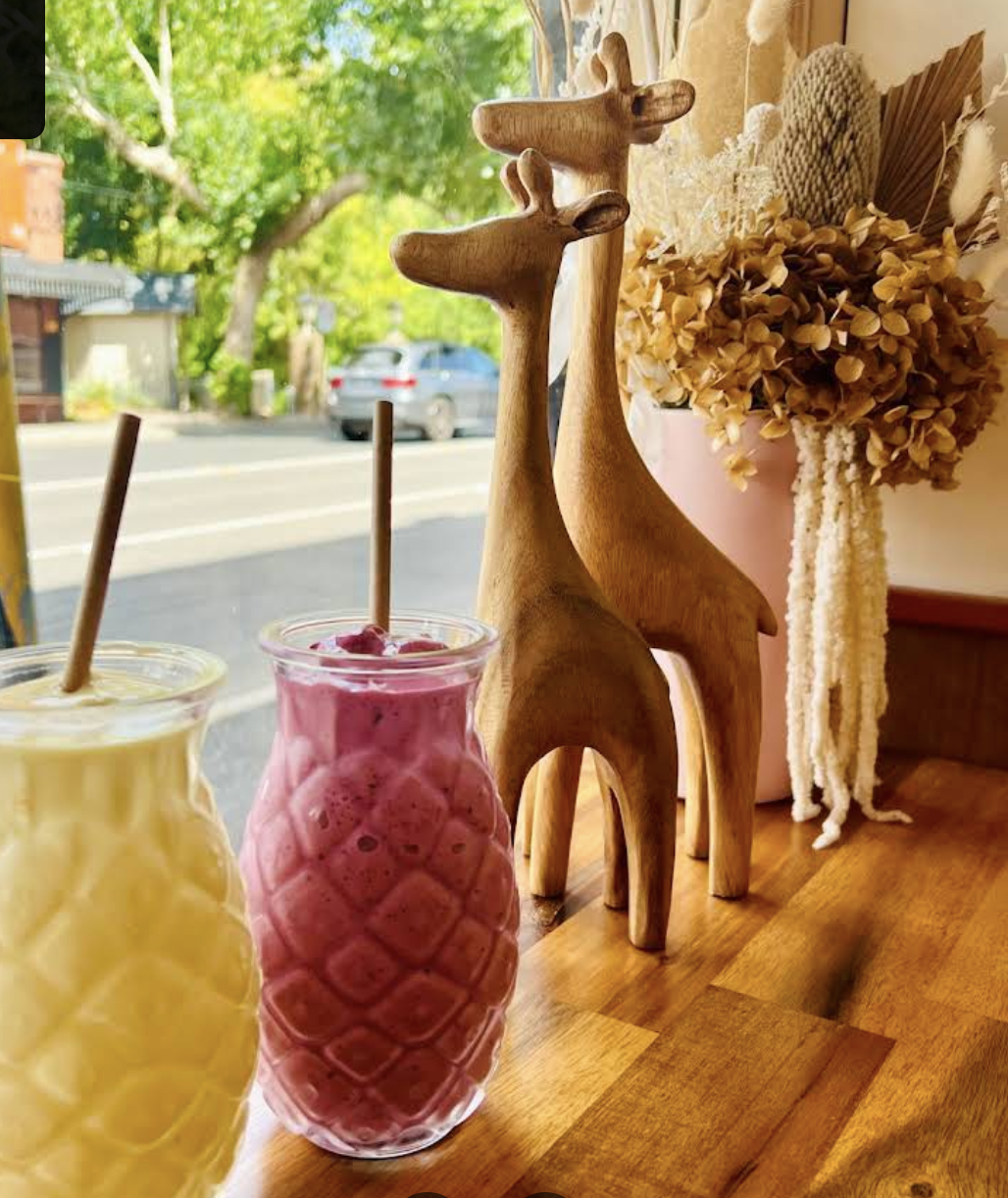 Pineapple-textured smoothie glasses on a timber bench, with two wooden giraffe ornaments